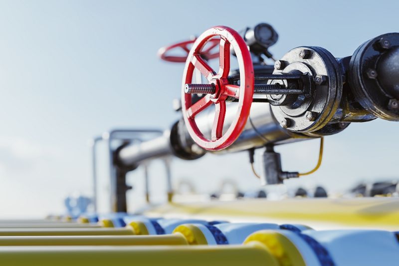 Silberfarbene Gasleitung mit Ventilhahn und rotem Handrad, die in den Hintergrund führt, am unteren Bildrand mehrere parallel laufende gelbe Leitungen.