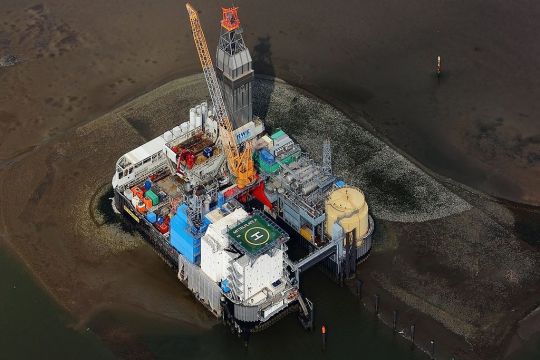 Luftaufnahme der rechteckigen Bohrplattform, eng bestückt mit Anlagen zur Ölförderung im Wattenmeer.