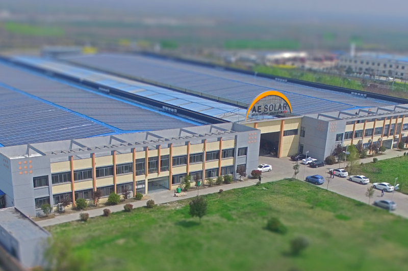 Große Fertigungshalle, über dem Eingang steht AE Solar mit dem Firmenlogo, davor einige Menschen und Autos.