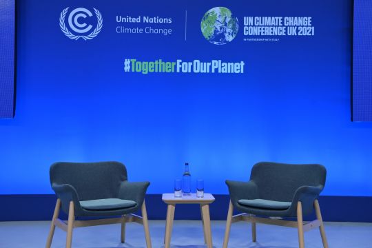 Zwei leere Stühle vor einer blauen Wand mit dem Logo des Klimagipfels COP 26 in Glasgow, dazu der Slogan auf Englisch: Zusammen für unseren Planeten.