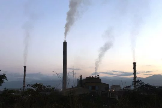 Graue Gebäude und Schornsteine der Nickelmine Fenix in Guatemala, aufgenommen in der Dämmerung.