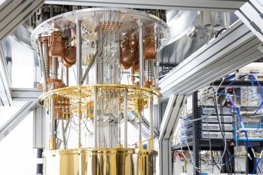 Kryogenischer Aufbau und Ansteuerung eines supraleitenden Quantencomputers - gold-, messing- und silberfarbene Leitungen, Schlingen und Röhrchen in einem zylinderförmigen metallischen Aufbau.