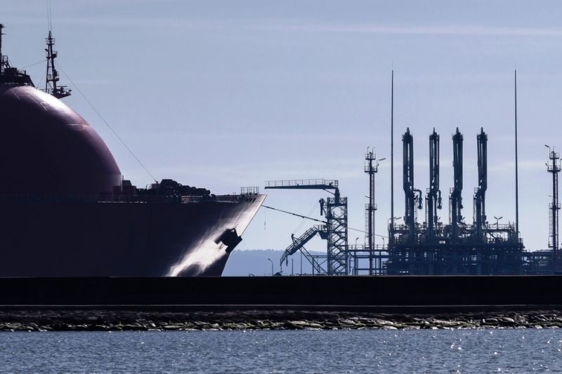 Dunkle Silhouette der Bugpartie eines LNG-Tankers an einem Flüssigerdgas-Hafen mit vier hoch aufragenden Entladearmen.