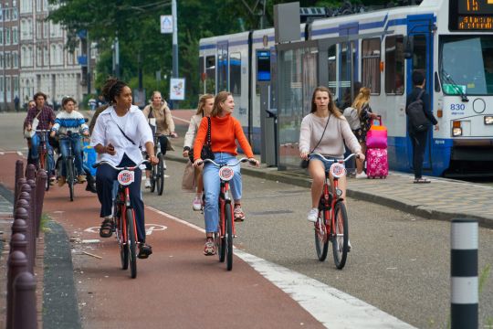 Radfahrerinnen auf einem breiten Radstreifen, etwas weiter daneben eine Straßenbahn.