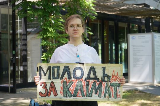 Ilyess El Kortbi steht vor dem Konferenzzentrum in Bonn und hält sein Schild hoch mit der ukrainischen Aufschrift: Jugend fürs Klima.
