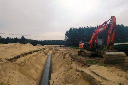 Erdgasleitung im Bau, neben dem ausgehobenen Graben, in dem schon ein Stück Rohr liegt, steht ein roter Bagger.