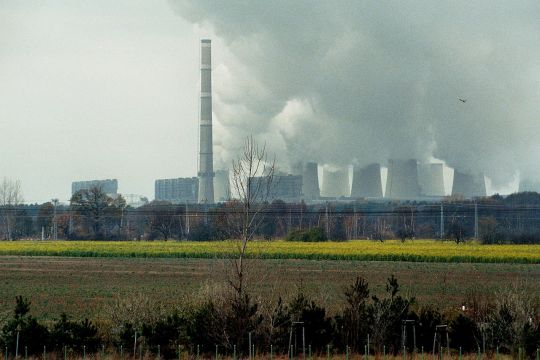 Braunkohlekraftwerk Jänschwalde mit stark dampfenden Kühltürmen hinter einem Feld. 