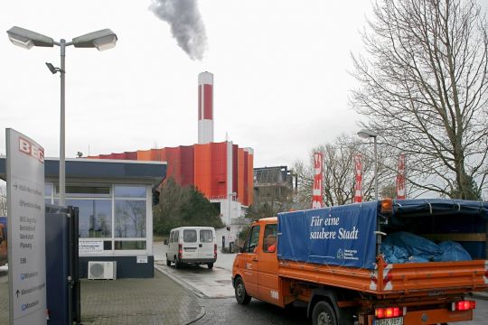 Ein Kleintransporter mit Müllsäcken fährt durch die Einfahrt zur Müllverbrennungsanlage Bremerhaven, im Hintergrund steht die freundlich angestrichene Anlage mit rauchendem Schornstein.