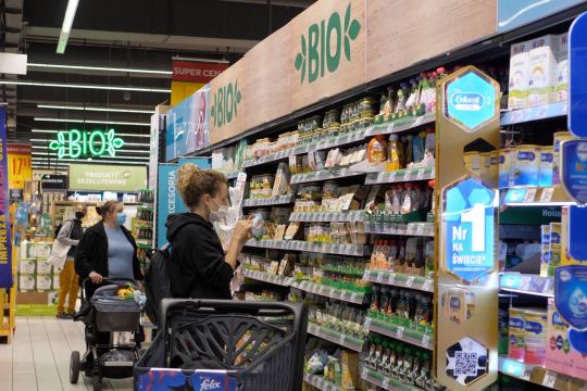 Eine Kundin mit Maske steht am Bio-Regal eines Supermarkts und studiert die Angaben auf einem Produkt.