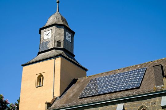 Kleine Kirche mit schiefergedecktem Turm und Solarpaneelen auf dem Dach, vermutlich im mitteldeutschen Raum.