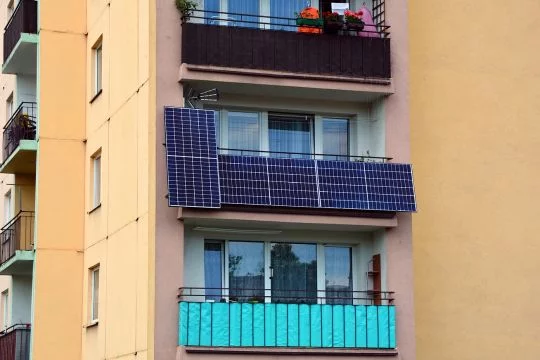 Drei übereinanderliegende Balkons an einem Plattenbau, der mittlere ist auf jeder möglichen Fläche mit Photovoltaik bestückt.