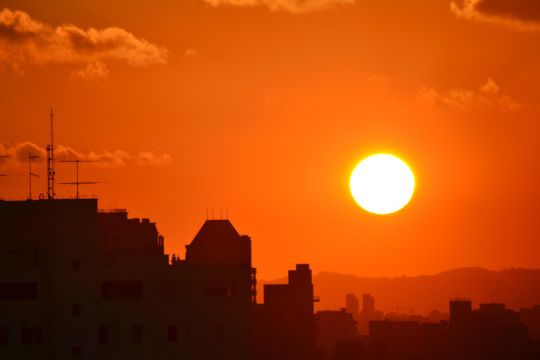 Sonne und orangeroter Himmel über den Dächern einer Stadt.