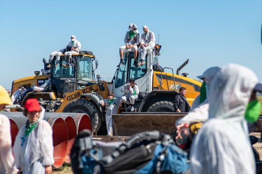 Weiß gekleidete Ende-Gelände-Aktivisten sitzen auf Baumaschinen, davor liegen Erdgasrohre.