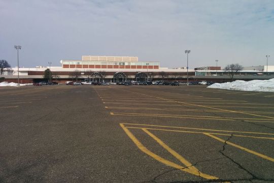 Riesiger, wenig belegter Parkplatz vor einem gesichtslosen Shopping Center.