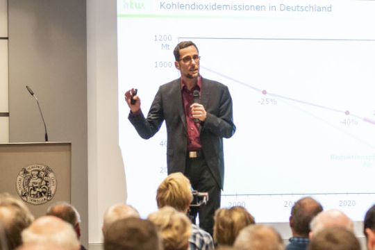 Volker Quaschning steht vor einer Grafik, spricht ins Mikro und gestikuliert mit der Hand.