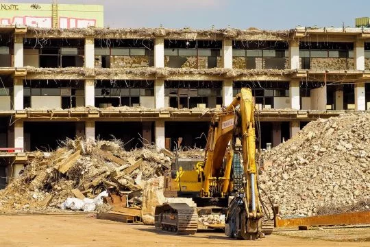 Ein gelber Bagger steht vor einem halb abgerissenen Plattenbau.