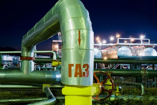 Auf einer grün gestrichenen Pipeline-Abzweigung vor nächtlicher Kulisse steht auf Russisch: Gas.