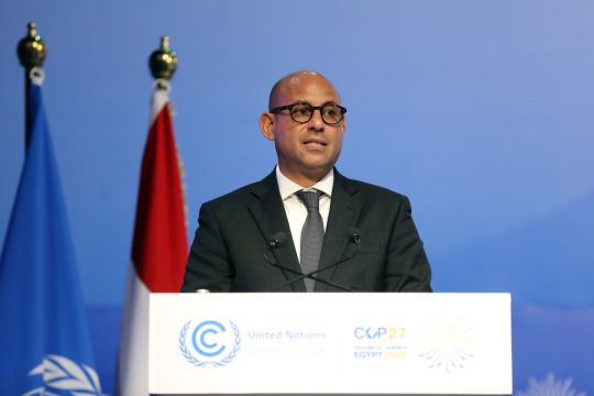 Simon Stiell steht an einem weißen Pult mit dem LOGO der COP 27 und spricht.