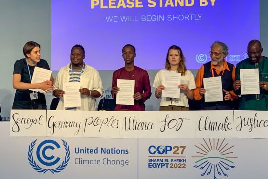 Vertreter:innen deutscher und senegalesischer Klimaschutzgruppen stehen auf dem Podium und halten die Gründungsurkunde einer neugegründeten Klima-Allianz hoch.