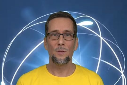 Volker Quaschning im gelben T-Shirt - im Hintergund ein stilisierter Atomkern mit darum kreisenden Elektronen.