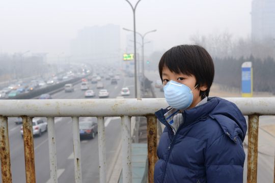 Junge mit Atemschutzmaske steht auf einer Brücke über die Stadtautobahn in Peking.