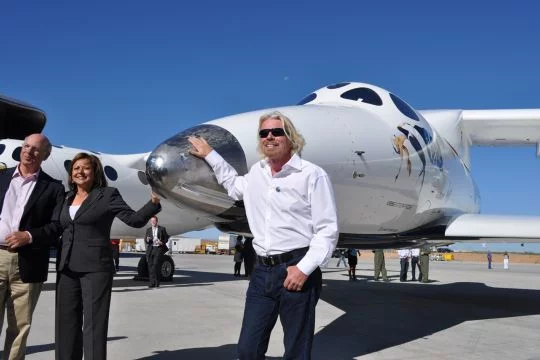 Richard Branson, Gouverneurin Susana Martinez und der Kongressabgeordnete Steve Pearce stehen neben einem von Bransons Raumflugzeugen auf Bransons Weltraumhafen in New Mexico.