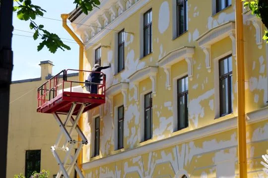 Zwei Bauarbeiter restaurieren eine gelbe Hausfassade.