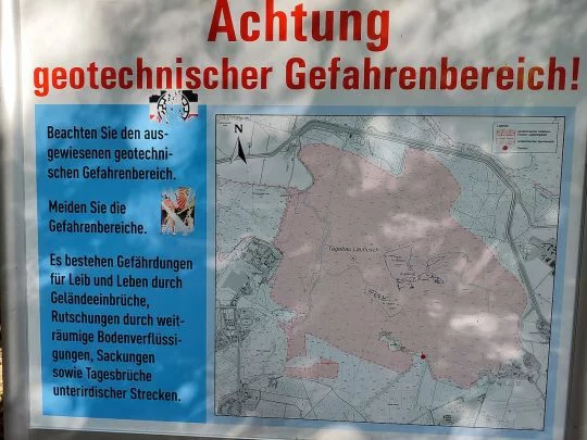 Schild mit einer Karte vom ehemaligen Tagebau Laubusch und der Aufschrift: Achtung – geotechnischer Gefahrenbereich! Es bestehen Gefährdungen für Leib und Leben durch Geländeeinbrüche, Rutschungen durch weiträumige Bodenverflüssigungen, Sackungen sowie Ta