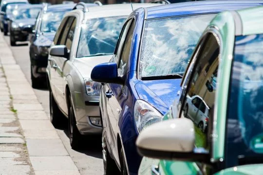 Autos stehen hintereinander am Straßenrand, man sieht keine Menschen. 