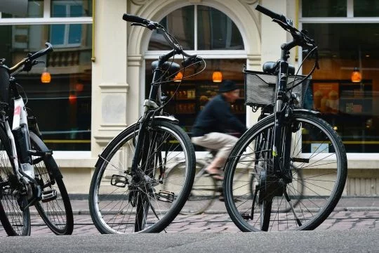 Drei Fahrräder sind am Straßenrand quer zur Fahrtrichtung abgestellt, möglicherweise auf einem Auto-Parkplatz.