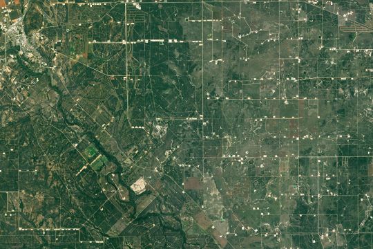 Satelliten-Aufnahme einer von Fracking-Bohrstellen und Verbindungsstraßen schachbrettförmig durchzogenen grünen Landschaft in Texas.