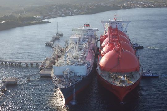 LNG-Schiff mit vier großen runden Tanks liegt längsseits an einem gleich großen Schiff, das als schwimmendes Terminal dient.