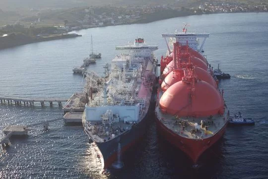 LNG-Schiff mit vier großen runden Tanks liegt längsseits an einem gleich großen Schiff, das als schwimmendes Terminal dient.
