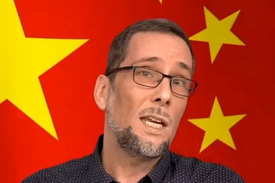 Aufmacherbild: Volker Quaschning vor einer China-Fahne, diese ist rot mit gelben Sternen.