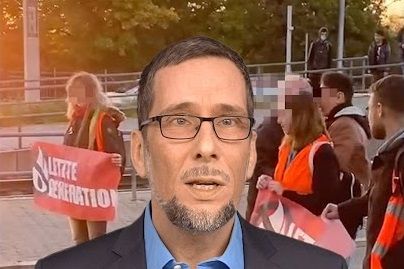 Volker Quaschning redet eindringlich, hinter ihm ist eine Straßenblockade der Gruppe Letzte Generation zu sehen.