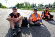 Ein älterer und zwei jüngere Männer in rosa Warnwesten sitzen auf der Autobahn A 100 in Berlin.