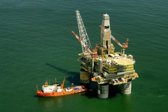 Bohrplattform im Meer, daneben ein kleineres Schiff.