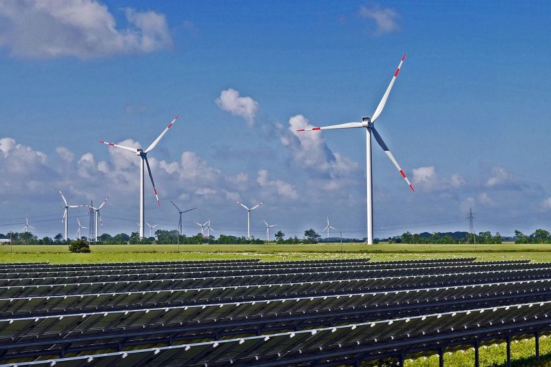 Windpark und Solarpark in flacher Landschaft bei heiterem Himmel.