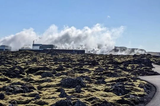 Geothermiekraftwerk auf einer kargen Ebene in Island, Dampfwolken steigen auf.