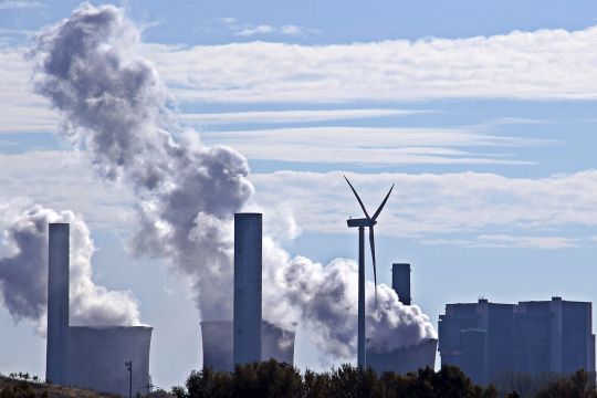 Dampfende Kühltürme der Blöcke eines Kohlekraftwerks im Rheinland und ein einzelnes Windrad.