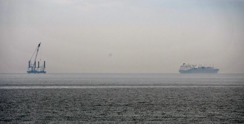 Eine Plattform und in einiger Entfernung ein Schiff etwa einen Kilometer vor der Küste, das Wetter ist diesig.