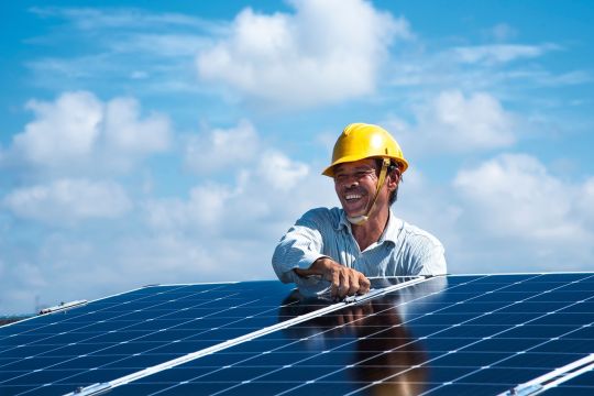 Lachender vietnamesischer Solarmonteur mit gelbem Helm bei der Arbeit.