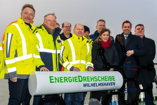 Politprominenz aus Bund, Land Niedersachsen und der Stadt sowie der Chef von Uniper stehen hinter einem Röhrenstück mit der Aufschrift: Energiedrehscheibe Wilhelmshaven.