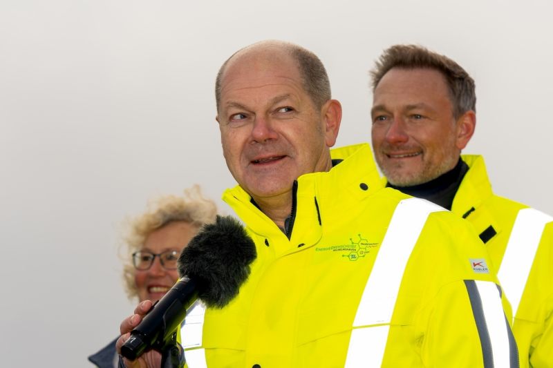 Olaf Scholz in gelber Windjacke spricht ins Mikrofon, hinter ihm Christian Lindner.