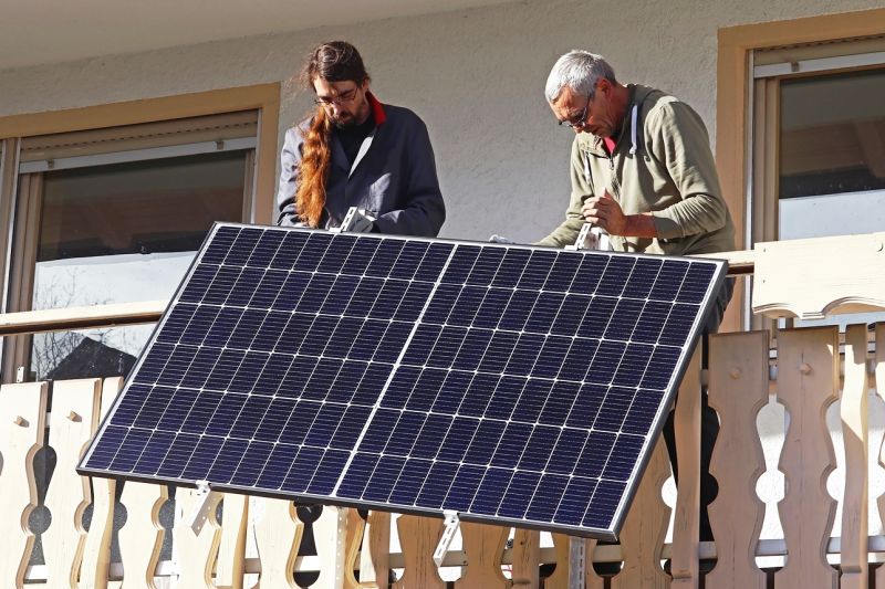 Ein junger und ein alter Mann stehen auf einem Balkon und schrauben zwei Solarmodule an.