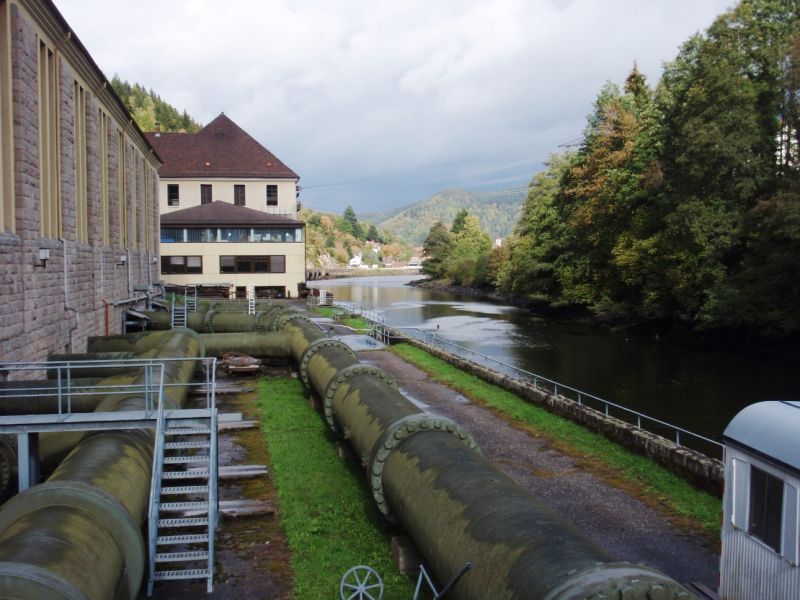 Große Wasserrohre zwischen dem Gebäude des Wasserkraftwerks und dem Fluss.