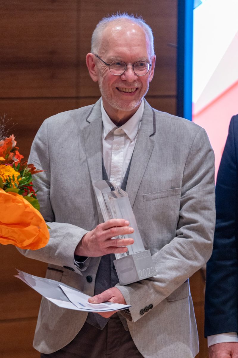 Joachim Wille hält den Journalistenpreis und einen Blumenstrauß in der Hand und freut sich.