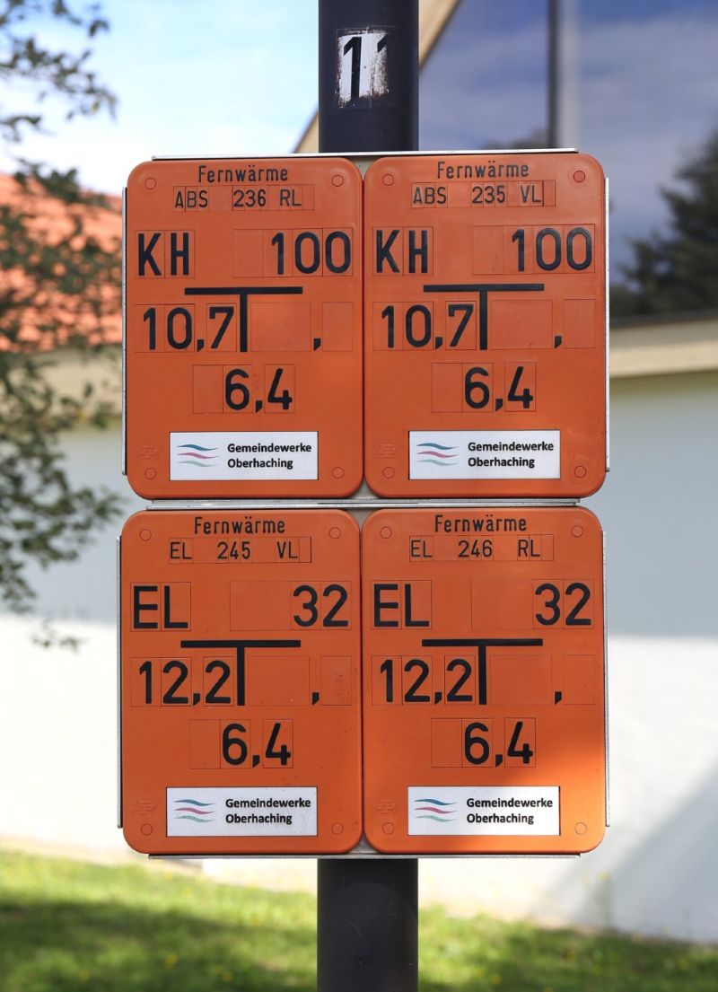 Vier Fernwärme-Hinweisschilder in Orange an einem Metallpfosten in Oberhaching bei München.