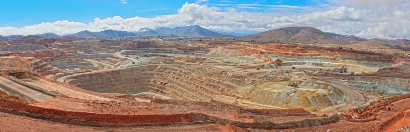 Panorama-Aufnahme einer riesigen Kupfermine, man sieht nur, gelblichbraune, in Stufen abgebaggerte Bergbaulandschaft und darüber den Himmel.