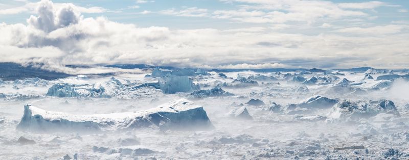 Luftaufnahme einer Eislandschaft mit zerklüfteten Eisbergen, Nebel und Wolken.